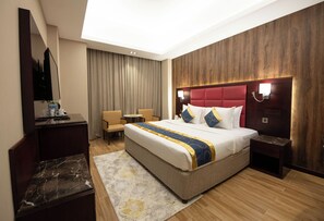 A hotel room with a large bed, a desk, a chair, a small table, and a TV. - Ramee Guestline Hotel (Muscat)