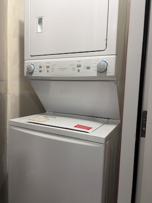Máquina de lavar frontal com painel de controle, etiqueta de aviso vermelha e porta.