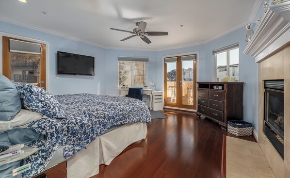 A bedroom with a bed, a desk, a chair, a TV, a ceiling fan, and a fireplace.