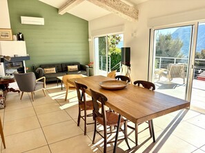 A dining area with a wooden table and chairs, a sofa with cushions, a television, and a view of the outdoors. - Villa toulon air-conditioned panoramic sea view swimming pool jacuzzi sauna (Toulon)