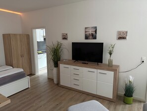 Una sala de estar moderna con un televisor de pantalla plana, un mueble de madera, una planta en maceta y una mesita.