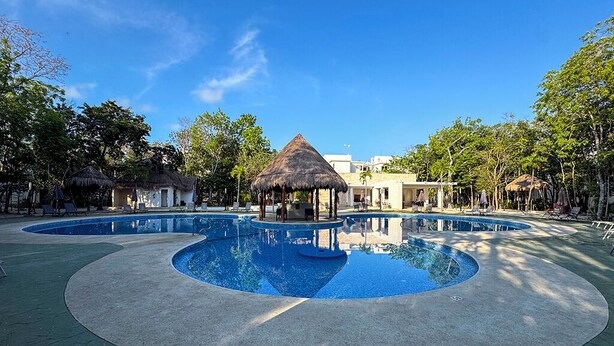 A circular pool with a central gazebo, surrounded by lounge chairs and shaded areas, with buildings in the background. - Xíinbal House in Puerto Morelos (Puerto Morelos)