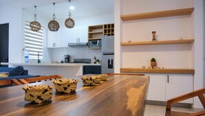 A modern kitchen with white cabinets, a wooden dining table, and hanging pendant lights. - Xíinbal House in Puerto Morelos (Puerto Morelos)
