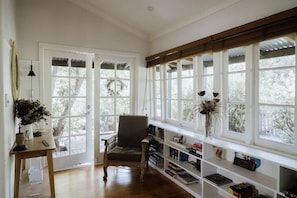 A room with a wooden floor, a chair, a bookshelf, and large windows with a view of trees.