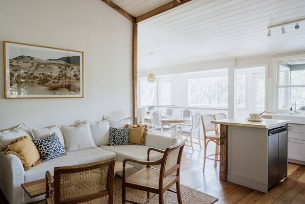 A cozy living room with a sofa, chairs, a dining table, and a kitchen area with a sink and cabinets.