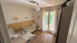 A baby room with a crib, changing table, and a window with curtains. - Quiet villa with pool close to the sea (Marsillargues)