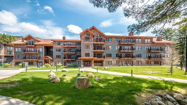 A multi-story hotel with a stone facade, balconies, and a well-maintained lawn with rocks.
