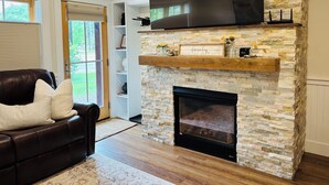 A living room with a stone fireplace, a mounted TV, and a leather sofa.