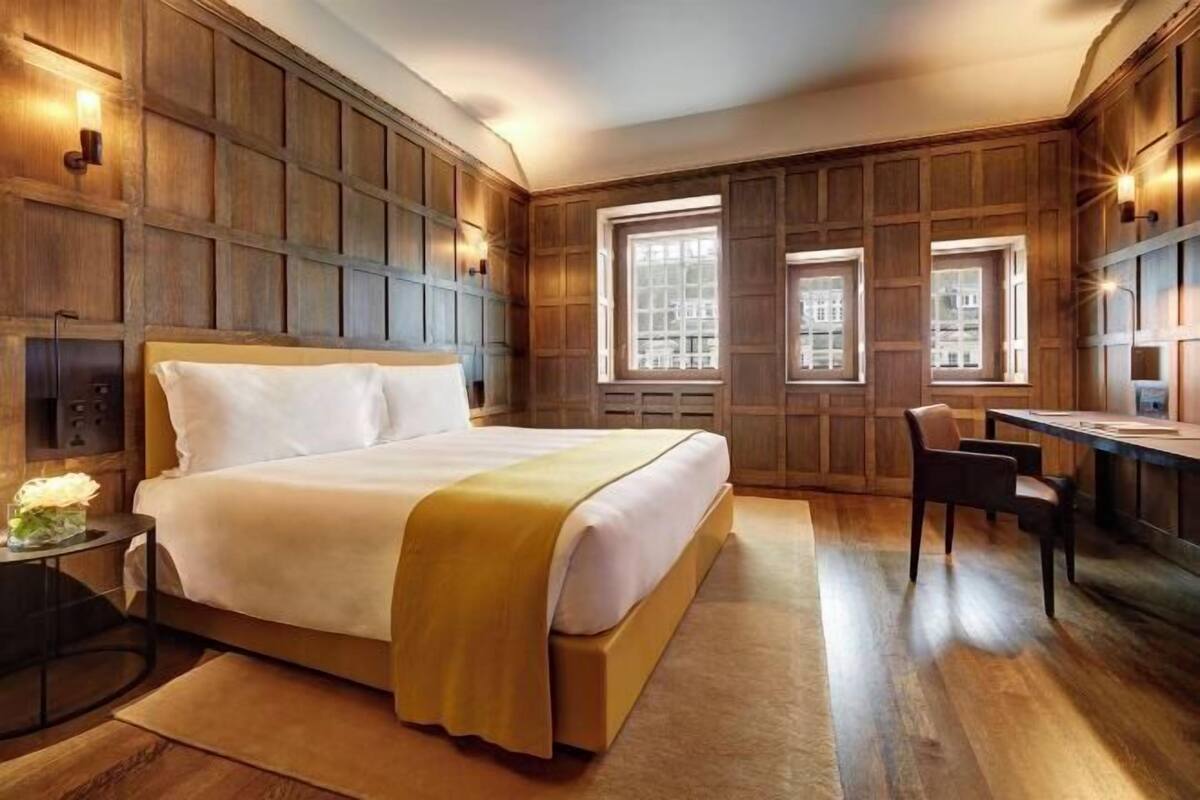 A bedroom with a large bed, wooden paneling, a desk, and two windows.