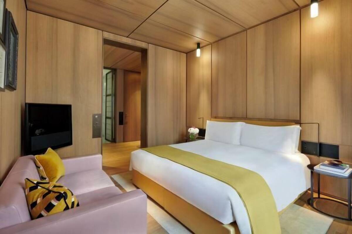A modern hotel room with a bed, a sofa, a TV, and a small side table.