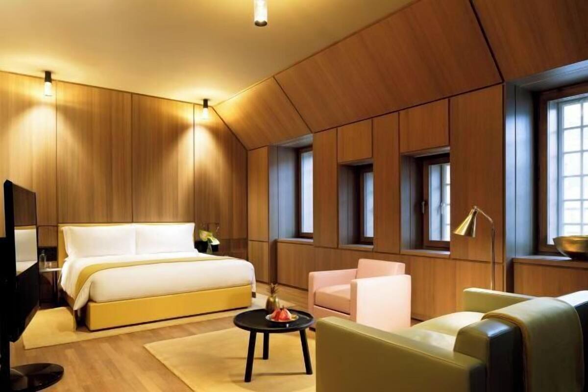 A modern hotel room with a large bed, a seating area, and a television.