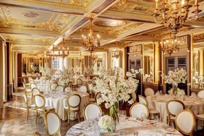 A grand banquet hall with round tables, gold accents, and chandeliers. - Hotel Cafe Royal (London)