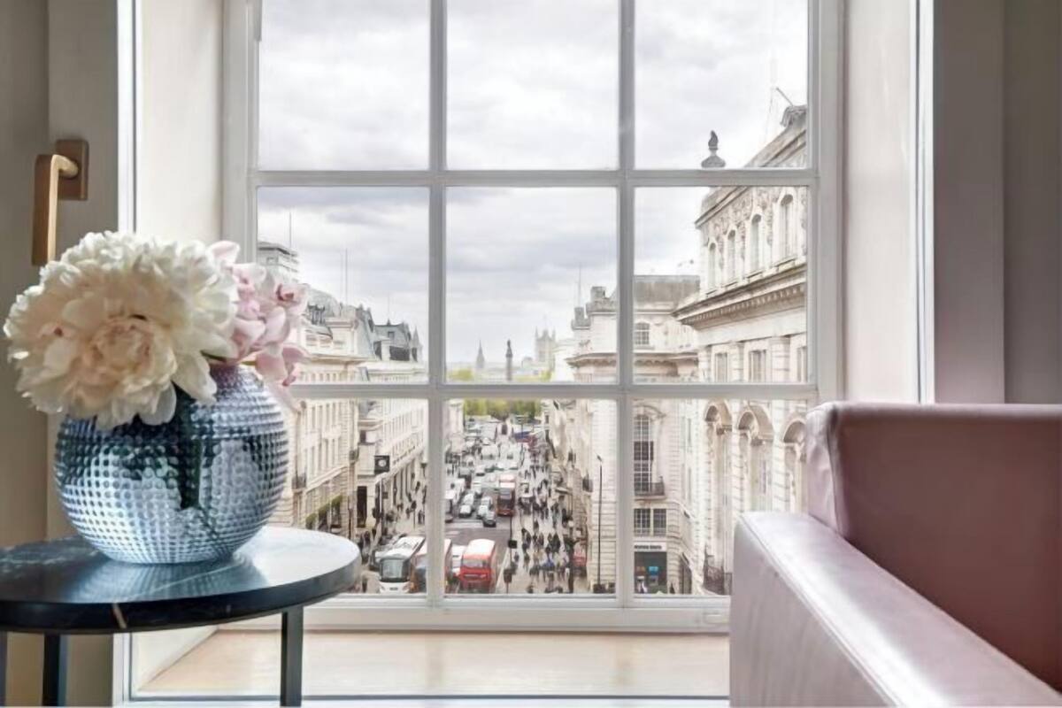 A window with a view of a city street, a vase with flowers, and a sofa.