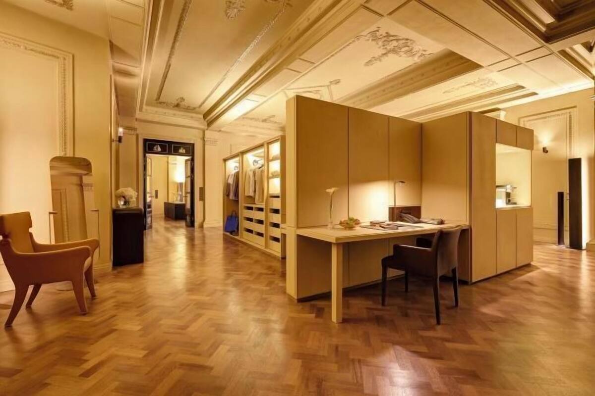 A hotel room with a wooden floor, a desk with a lamp, a chair, and a wardrobe.