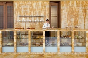 A bakery counter with a chef, displaying pastries and baked goods in glass cases. - Hotel Cafe Royal (London)