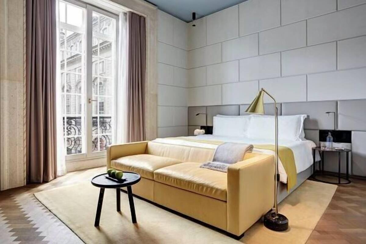 A modern hotel room with a large bed, a sofa, a small table, and a floor lamp.