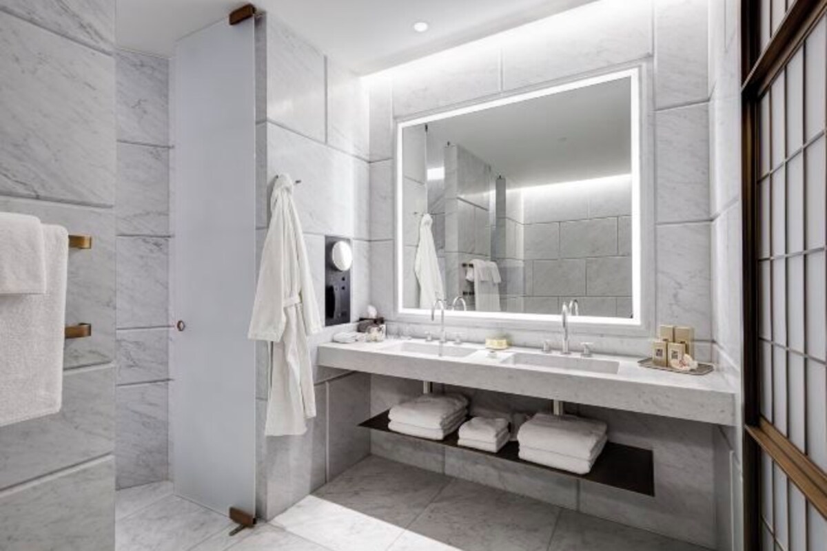 A modern bathroom with a large mirror, two sinks, and a shower area.