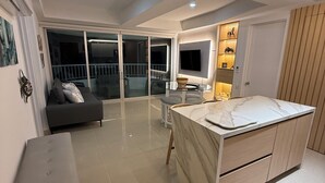 A modern living room with a sofa, a small table, and a kitchen area with a marble countertop.