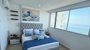 A modern bedroom with a large bed, a bedside table, a nightstand, a window with a view of the sea, and a ceiling light.