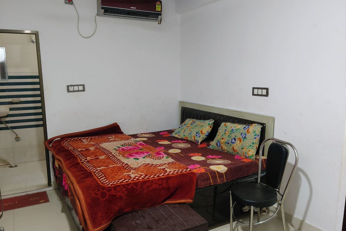 A bedroom with a bed, a chair, a bench, and an air conditioning unit.