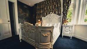 A bedroom with a large ornate bed, a nightstand, and a window with curtains. - Cbh Ruthin Castle Hotel and Spa (Ruthin)
