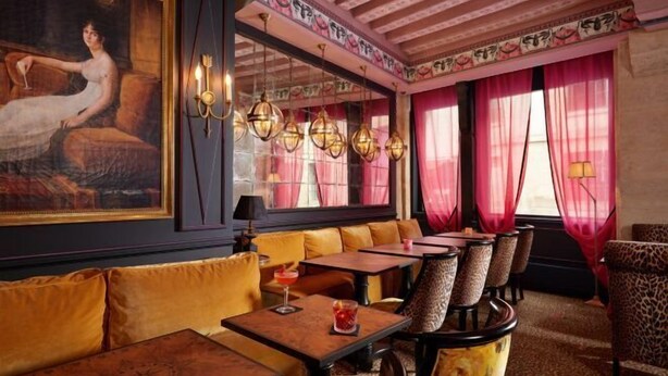 Un restaurant au décor classique, avec un grand tableau au mur, de nombreuses tables avec des chaises et un plafond orné de motifs.