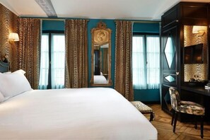 A hotel room with a large bed, a desk, and a chair. There is a mirror on the wall and curtains on the windows. - JOBO hotel - Joséphine Bonaparte (Paris)
