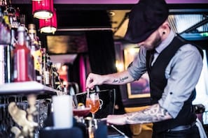 Un cantinero preparando una bebida en la barra, con estantes llenos de botellas y vasos.