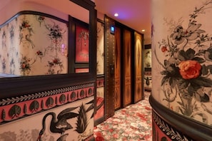 A hallway with floral wallpaper, a mirror, and a door with a decorative frame. - JOBO hotel - Joséphine Bonaparte (Paris)