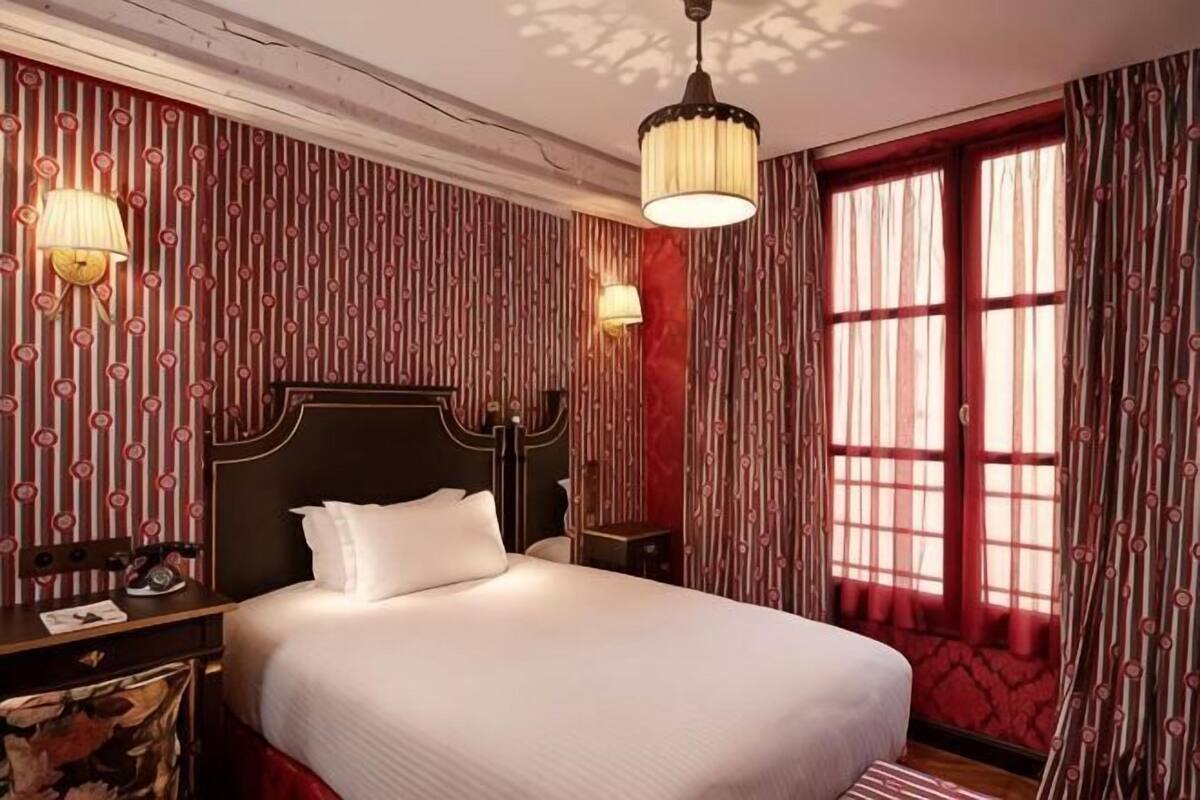 A hotel room with a large bed, a nightstand, a lamp, and a window with curtains.