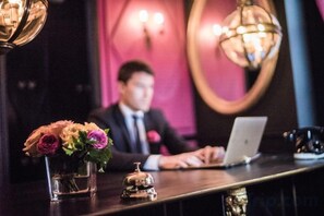 A reception desk with a laptop, a vase with flowers, and a bell. - JOBO hotel - Joséphine Bonaparte (Paris)
