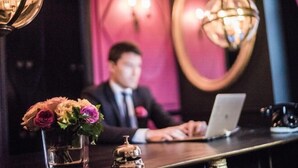 Un comptoir d’accueil avec un ordinateur portable, un vase de fleurs et une cloche.