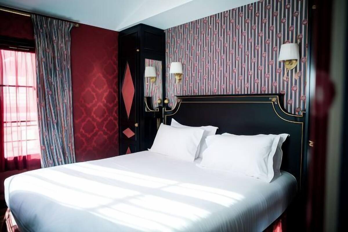 A hotel room with a large bed, a dark headboard, and patterned wallpaper.