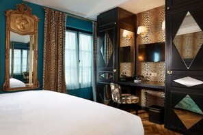 A hotel room with a large bed, a desk with a chair, a mirror, and a patterned wall. - JOBO hotel - Joséphine Bonaparte (Paris)