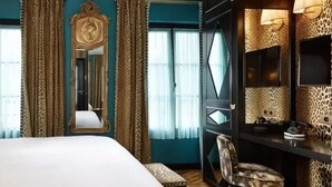 Une chambre d’hôtel avec un lit, un bureau, une chaise, un miroir et une fenêtre avec des rideaux.