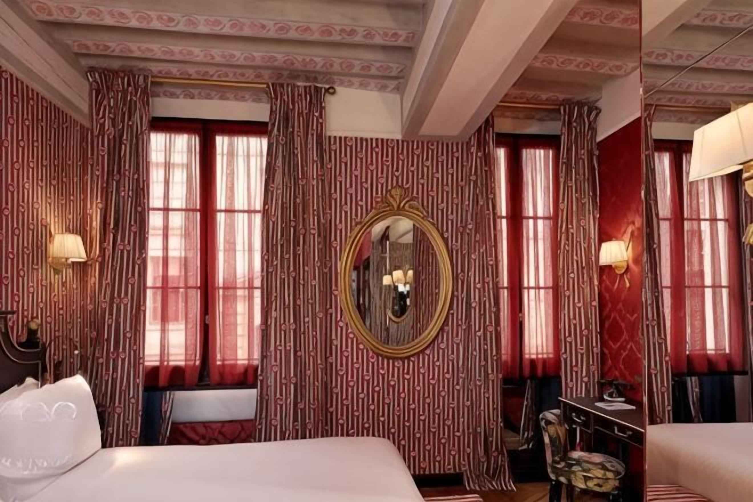 A hotel room with a large bed, a mirror, curtains, and a lamp.