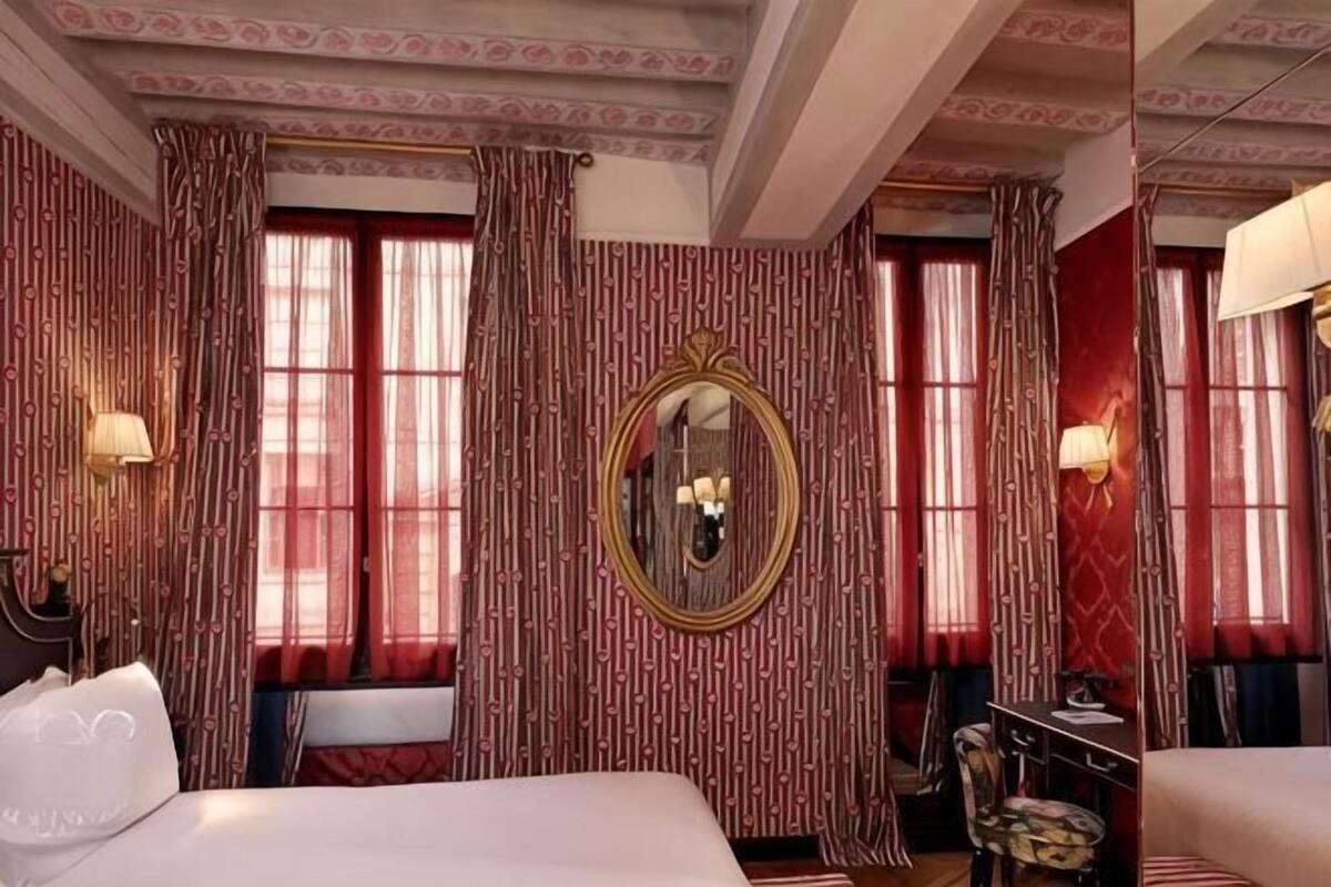 A hotel room with a large bed, a mirror, curtains, and a lamp.