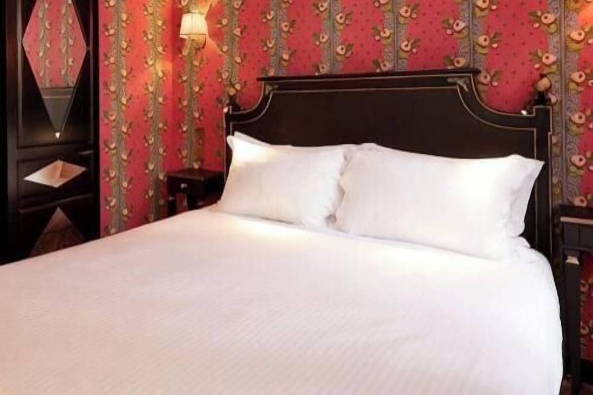 A bed with white linens, a dark wooden headboard, and a wall with floral wallpaper.