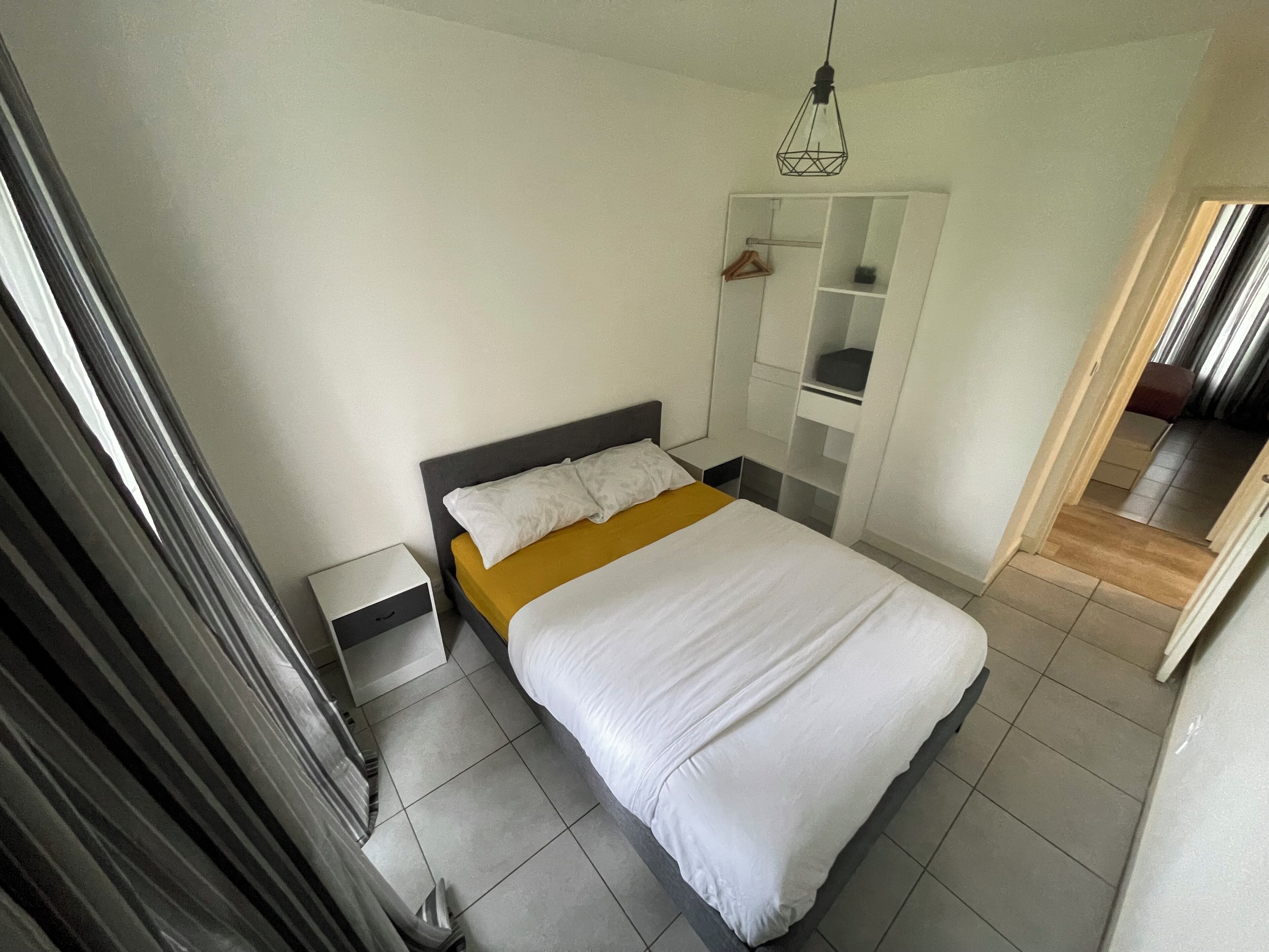 A modern bedroom with a bed, a nightstand, a wardrobe, and a hanging light fixture.