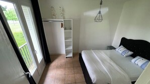 Ein Schlafzimmer mit Bett, Kleiderschrank, einer Pendelleuchte und Blick ins Freie.