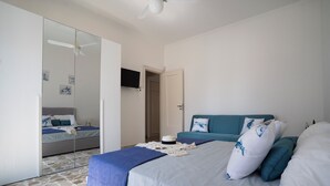 A bedroom with a bed, a blue sofa, a wardrobe, and a ceiling fan. - At 30 MT from the sea Apartment 6 places in Aci Trezza (Aci Castello)