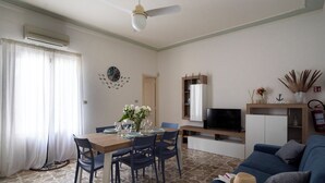 A living room with a dining table, chairs, a sofa, a TV, and a ceiling fan. - At 30 MT from the sea Apartment 6 places in Aci Trezza (Aci Castello)