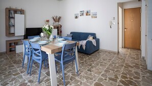 A dining area with a wooden table set for four, blue chairs, a blue sofa, and a stone-tiled floor. - At 30 MT from the sea Apartment 6 places in Aci Trezza (Aci Castello)