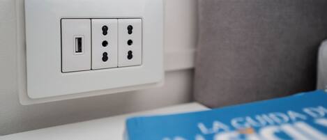 Une prise électrique blanche dotée d’un port USB et de trois prises standard, située à côté d’un rideau gris.