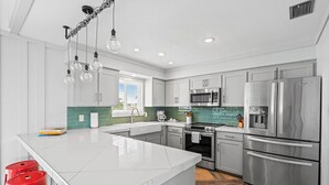 Una cocina moderna con armarios blancos, electrodomésticos de acero inoxidable y una isla central con taburetes.