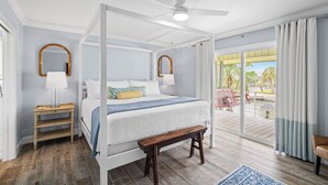 Una cama con dosel y cuatro postes, un banco de madera, una mesita de noche y vistas a una terraza exterior con mesa y sillas.