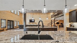 Eine moderne Küche mit einer großen Granitarbeitsplatte, einem schwarzen Spülbecken und drei Pendelleuchten.