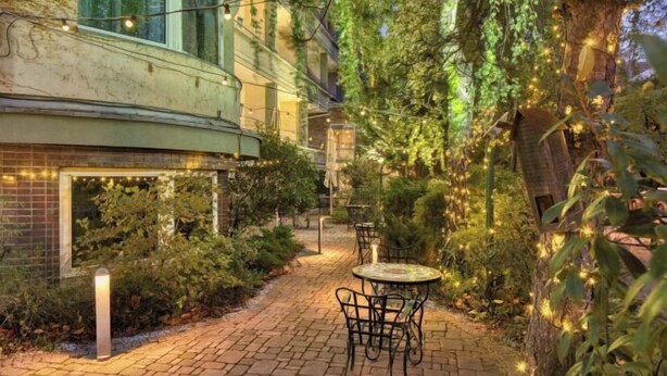 A paved outdoor area with a table and chairs, surrounded by greenery and string lights. - Mamaison Hotel Andrassy Budapest (Budapest)