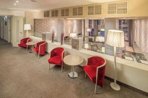 Un hall d’hôtel avec des fauteuils rouges, une table ronde et un grand lampadaire.