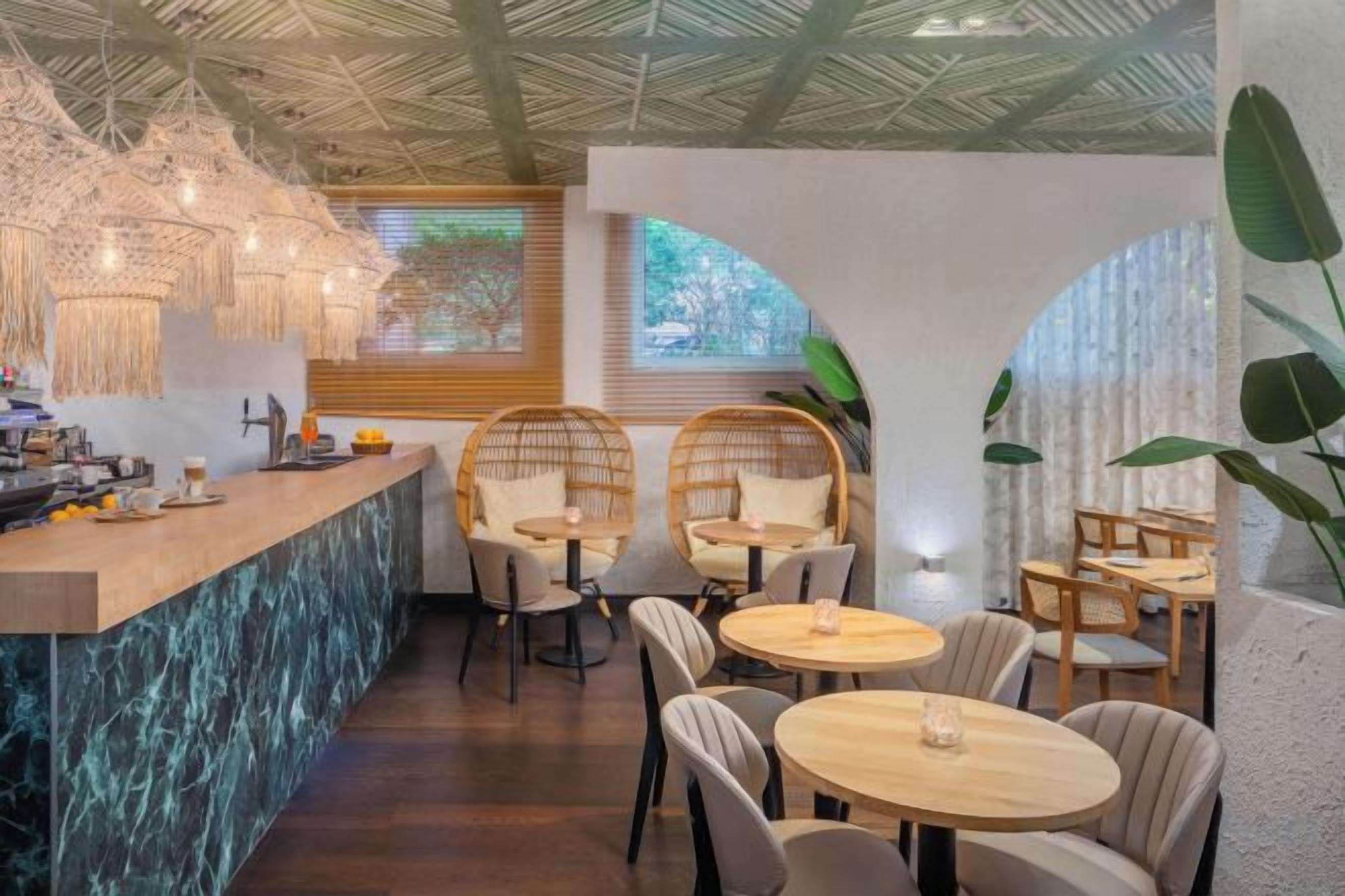 A restaurant with a bar area, round tables, and wicker chairs.